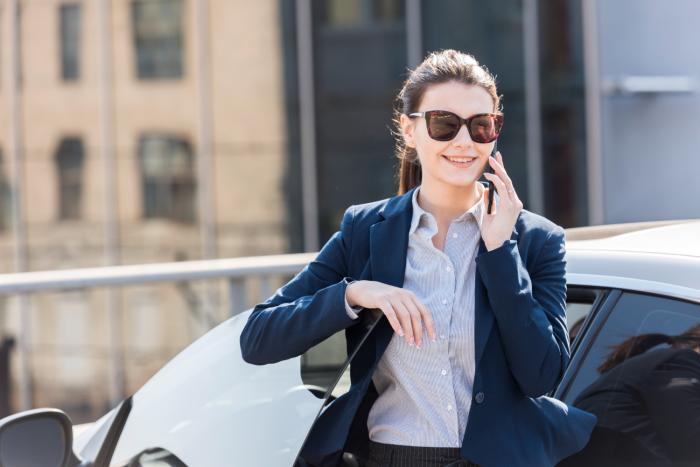 businesswoman talks on phone while standing next to car financial advisor transitions