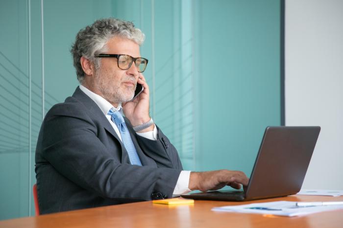 older financial advisor working on laptop in office while talking on the phone financial advisor transitions